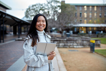 Young Asian student holding her laptop on lawn at university campus