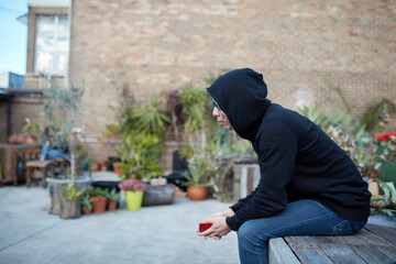Man sitting in courtyard wearing black hoodie and sunglasses