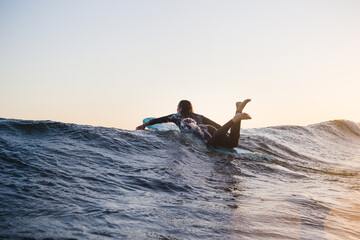 Woman surfing on surfboard in sea during sunset
