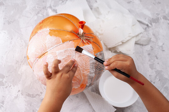 baby's hands makes a papier-mache pumpkin from a balloon, DIY for Halloween in isolation.