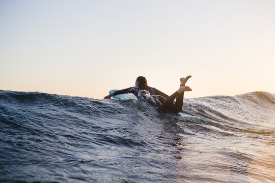 Woman surfing on surfboard in sea during sunset