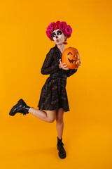 Amusing caucasian girl in halloween makeup posing with pumpkin
