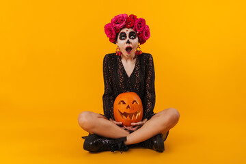 Shocked girl in halloween makeup with pumpkin sitting on floor