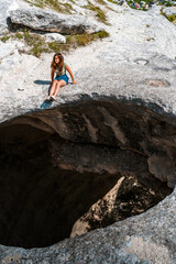 A young tourist girl is sitting on the edge of a huge hole in the cave. Picturesque mystical natural phenomenon in the Crimea