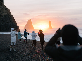 Tourists photographing the sunrise at Reynisfjara black sand beach in winter. South coast of Iceland.