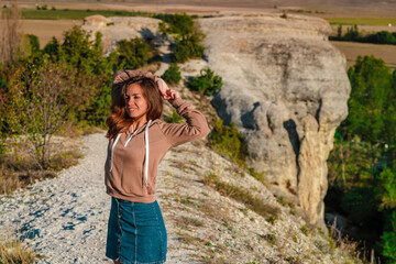 Naklejka premium Young woman in a jacket poses and smiles while standing on a mountain hill, a healthy lifestyle concept