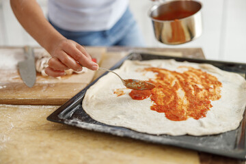 Beautiful smily handsome woman is preparing tasty fresh italian pizzawith vegetables at her kitchen at home