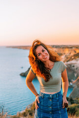 Attractive young woman posing against the blue sea and mountains at sunset. The concept of romance, travel and tourism