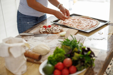 Beautiful smily handsome woman is preparing tasty fresh italian pizzawith vegetables at her kitchen at home