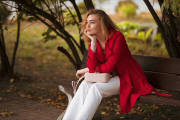 Woman in red coat sitting on bench in autumn park