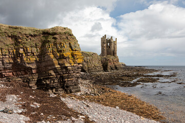 The ruins of Keiss castle photographed on a sunny day from a rocky beach.