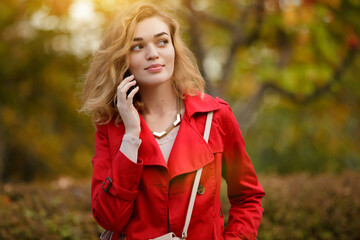 Woman in red coat talks by phone at autumn park