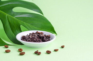 natural herbal cosmetic product for skin care. sugar, salt scrub with ground coffee and beans for face, body for massage, exfoliationwith monstera leaf on green background, copy space, text.