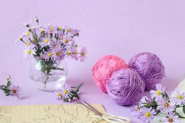 Skeins of multi - colored yarn - purple and pink ,with a bouquet of chrysanthemums and knitting...
