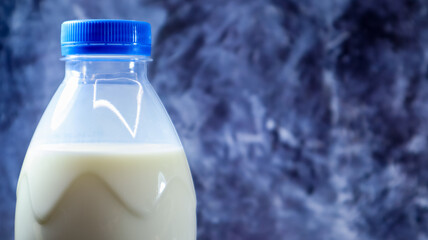 A plastic bottle of fresh regular milk on a dark gray marbled or concrete background. Close-up front view. World milk day concept. Nutrient fluid. Copy space.