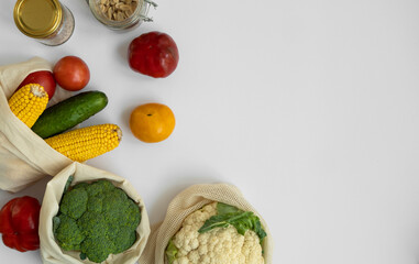 Vegetables in eco bag on white surface with a copy space. Pepper, tomato, corn, cucumber, broccoli, cauliflower in reusable shopping eco friendly cotton fabric bags. Zero waste plastic free concept.