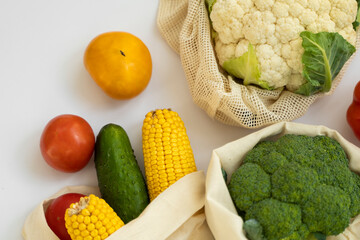 Vegetables in eco bag on white surface. Pepper, tomato, corn, cucumber, broccoli, cauliflower in reusable shopping eco friendly cotton fabric bags. Zero waste and plastic free concept. Sustainable.