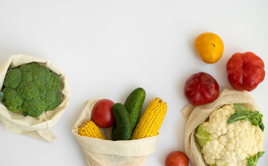 Vegetables in eco bag on white surface with a copy space. Pepper, tomato, corn, cucumber, broccoli, cauliflower in reusable shopping eco friendly cotton fabric bags. Zero waste plastic free concept.