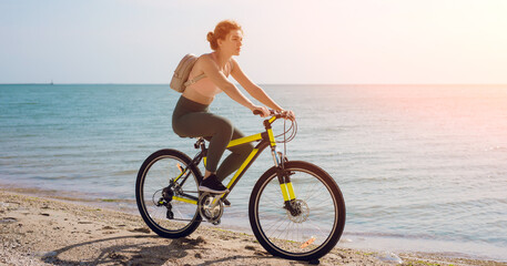 Fototapeta premium Young woman bicycling along a beach