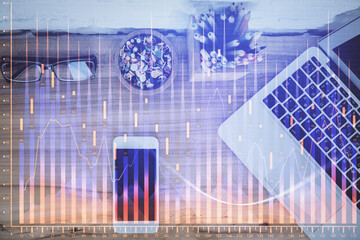 Double exposure of financial graph hologram over desktop with phone. Top view. Mobile trade platform concept.
