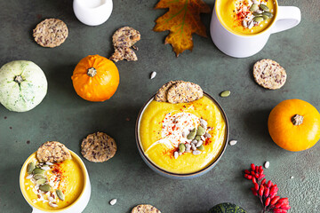 Roasted thick pumpkin vegetarian cream soup with pumpkin seeds, multigrain crackers and seeds on green stone background. Top view.