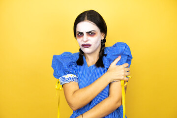 woman wearing a scary doll halloween costume over yellow background with pain on her shoulder and a painful expression