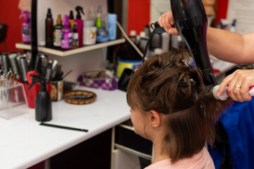 Beautiful teen girl at the hairdresser blow drying her hair after cutting it