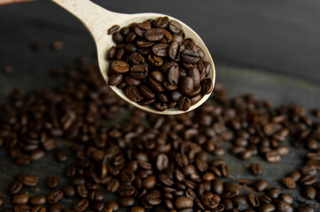 Fresh roasted arabica coffee beans in a wooden spoon and scattered coffee beans on a wooden table.