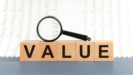 On wooden blocks under a magnifying glass text: VALUE. Educational concept