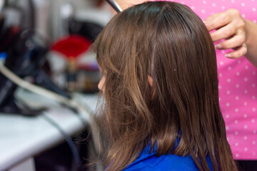Professional female hairdresser cutting girl's brown hair in salon, closeup
