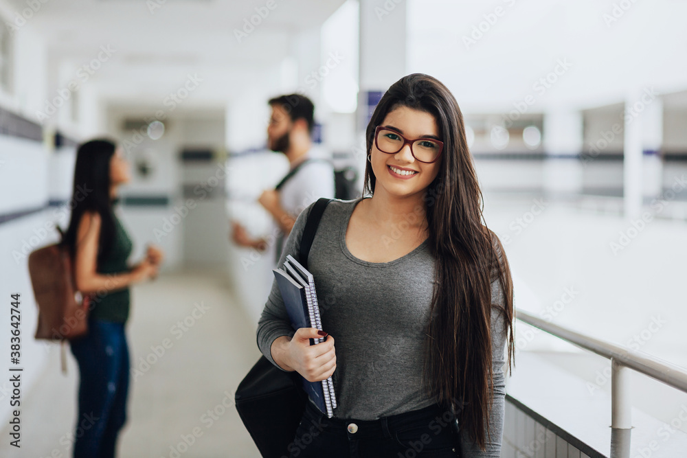 Wall mural Portrait of young Brazilian student with backpack carrying books in college.