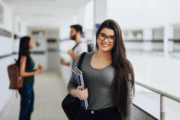 Portrait of young Brazilian student with backpack carrying books in college.