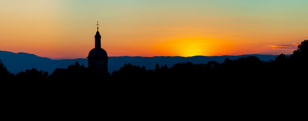 Obraz premium The stunning beauty and colors of the sunset overlooking the silhouettes of the Alps and the silhouette of a beautiful church