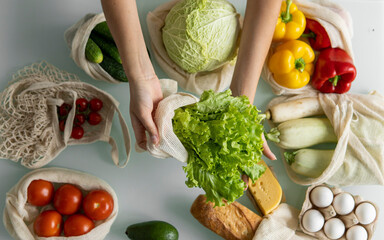 Woman's hand, holding a reusable grocery bag with vegetables on a kitchen at home and takes salad out. Zero waste and plastic free concept. Mesh cotton shopper with vegetables. Ecology.