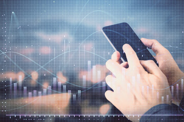 Double exposure of man's hands holding and using a digital device and forex graph drawing. Financial market concept.