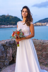 Fototapeta na wymiar Portrait of smiling young woman in white wedding dress on her wedding day by the sea