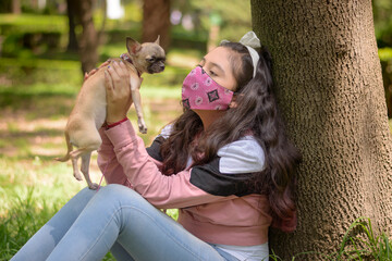 niña sentada en el pasto con  cubrebocas jugando en el pasto con su cachorro feliz en un dia...