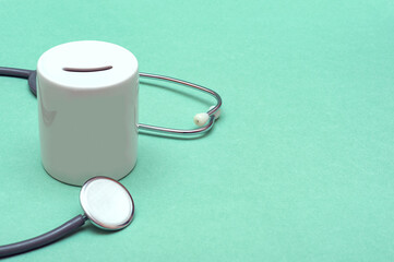Cost of healthcare. Money box with a medical doctors stethoscope on green background. Place for text. Copy space.
