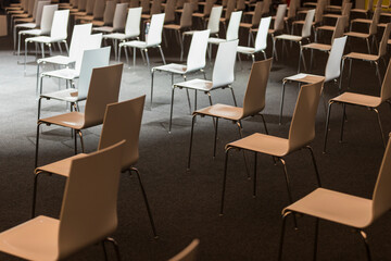 Group of white chairs arranged for social distance, ready to sit visitors in indoor business conference. COVID-19 health and safety measures during pandemic require spacing between people