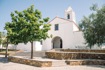 Fototapeta premium beautiful landscape of a small church built of white stone. little tree growing in front of the church. church in portugal. church with a tower with bells