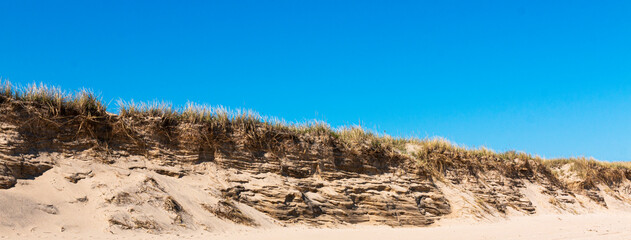 Battered sand dune on Montauk Beach with a deep blue sky
