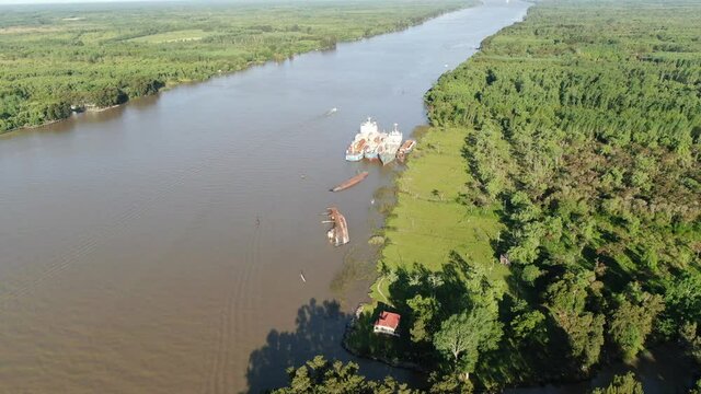 Vista desde un dron a lo largo de un ancho r&iacute;o con frondosas arboledas en la costa, barcos hundidos y amarrados. 