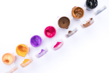 Pots of colorful paint in a paint set against white blank background with copy space pink purple orange brown a small child hand holding a paint brush dipping into paint pot macro close up