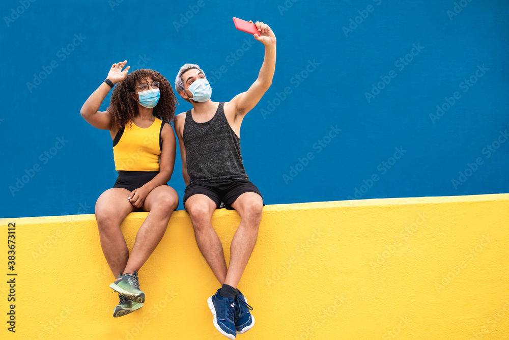 Wall mural young fitness black woman with a friend taking a selfie with mobile phone wearing face mask during c