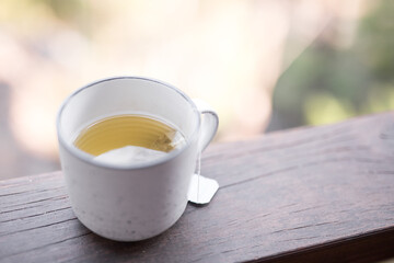 White simple ceramic herbal tea coffee mug herbal tea on a timber ledge outdoors against the blurred forest and trees natural background