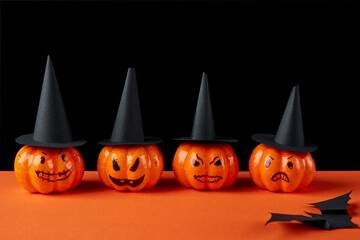 A row of decorative pumpkins in black hats on a black- orange background. Halloween holiday concept