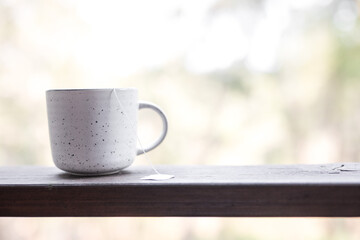 White simple ceramic herbal tea coffee mug herbal tea on a timber ledge outdoors against the blurred forest and trees natural background