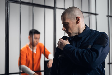 A prison guard in full ammunition communicates with his partner on the radio. In the background, a...