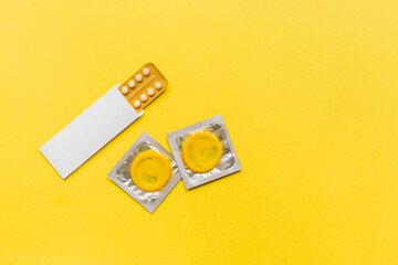 Composition with colorful condoms and birth control pills on yellow background. Safe sex and contraceptive concept. Flat lay, top view, copy space.