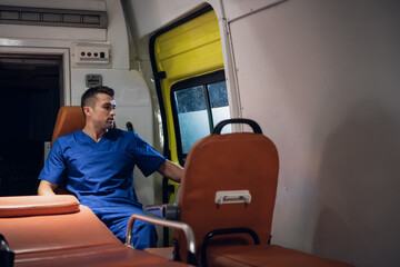 Man in a medical uniform sitting in an ambulance car and looking through the window.